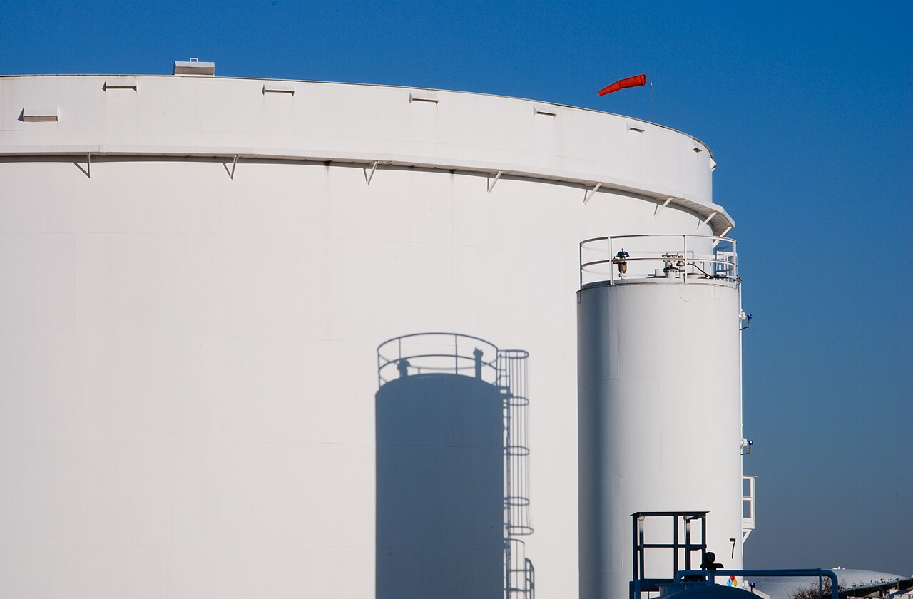 White cylindrical refinery storage tanks under a blue sky
